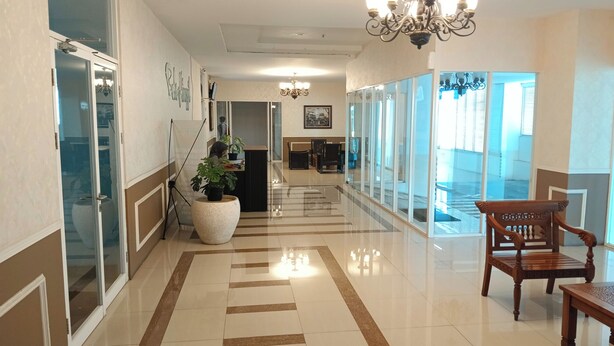 A hotel lobby with a long corridor, a reception desk, a large potted plant, a chandelier, and a wooden bench. - PLUM Dreamscape Bale Hinggil Surabaya (Surabaya)