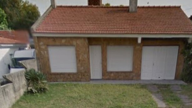 Une maison à deux étages avec un toit recouvert de tuiles rouges, un garage à l’avant et un petit jardin devant la maison.