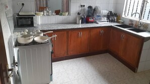 A kitchen with white tiled walls, a microwave, a stove, and wooden cabinets. - Spacious Family Home  (Arusha)