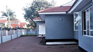 A residential area with a paved driveway leading to a house with a grey exterior and a red-tiled roof. - Spacious Family Home  (Arusha)