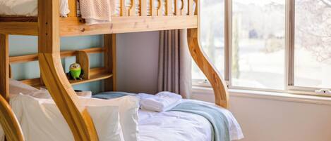 A bunk bed with a wooden frame, white bedding, and a view of a snowy landscape through a window.