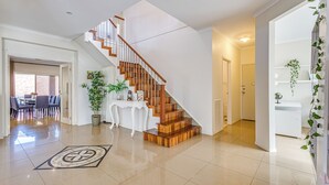 A spacious living area with a wooden staircase, a dining table with chairs, and a potted plant. - StayAU Family Home in Caroline Springs (Caroline Springs)