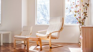 A modern room with two white chairs, a wooden floor, and a window with a view of trees. - StayAU Family Home in Caroline Springs (Caroline Springs)