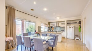 A modern kitchen with a dining area, featuring a glass table, grey upholstered chairs, and a small kitchen island. - StayAU Family Home in Caroline Springs (Caroline Springs)