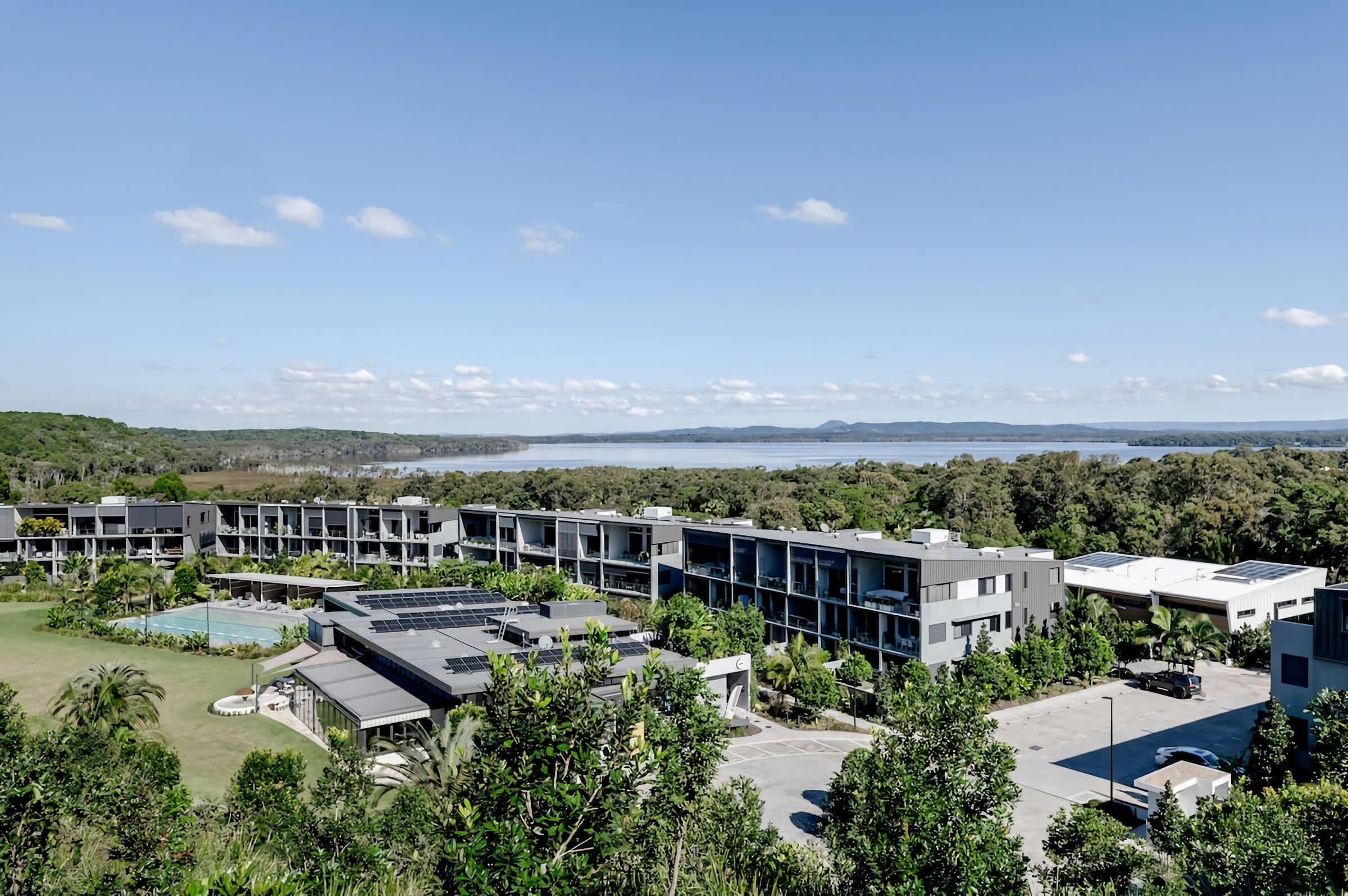 A modern building complex with multiple floors, a swimming pool, and a parking area.