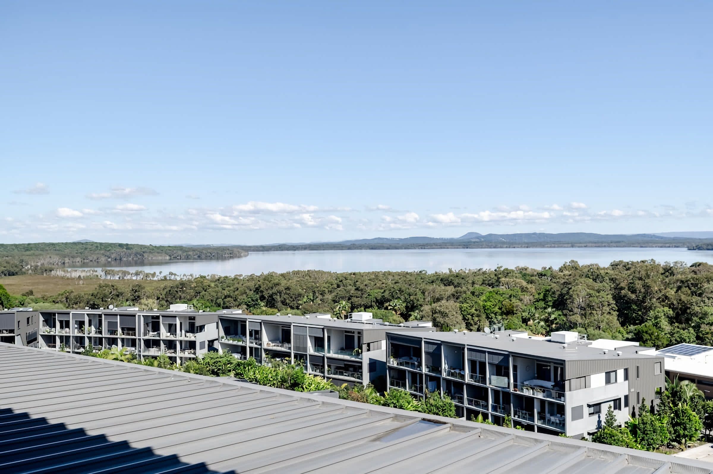 Un edificio moderno con varios balcones que dan a un lago y colinas boscosas.