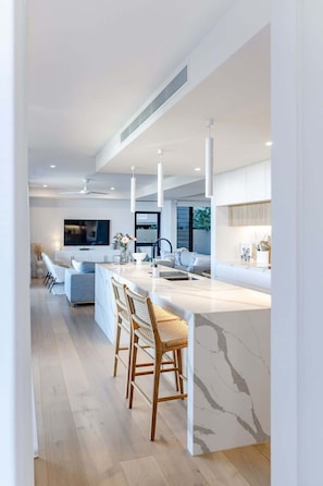 A modern kitchen with a marble island, bar stools, a large window, and a built-in TV.
