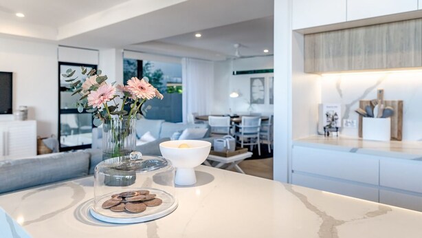A modern kitchen with a marble countertop, a vase with flowers, a bowl, and a plate of cookies.