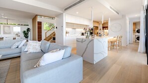 A modern living room with a grey sofa, a kitchen with a marble island, and a staircase leading to an upper level.