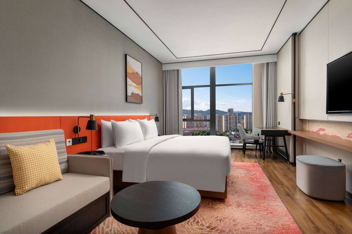 Una camera d'albergo moderna con un letto grande, un divano, una scrivania e una televisione.