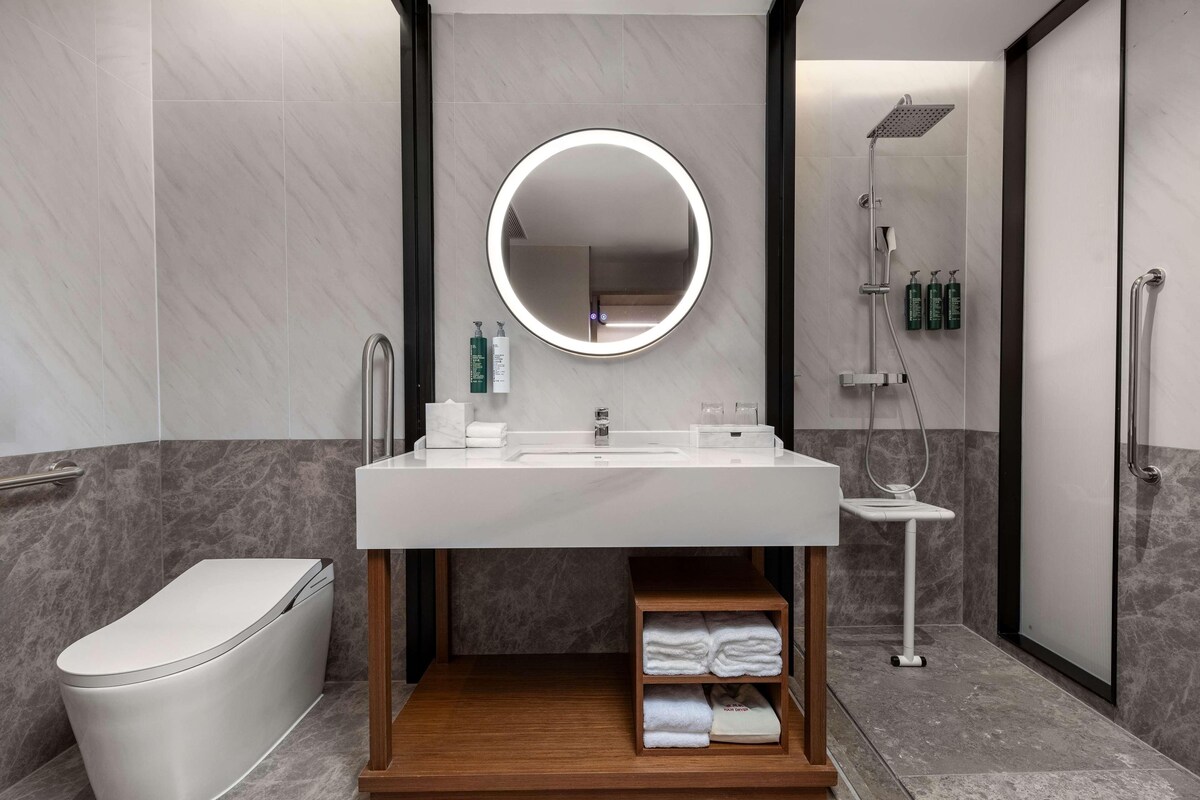 Un baño moderno con un espejo redondo, un lavabo, un inodoro y una ducha.