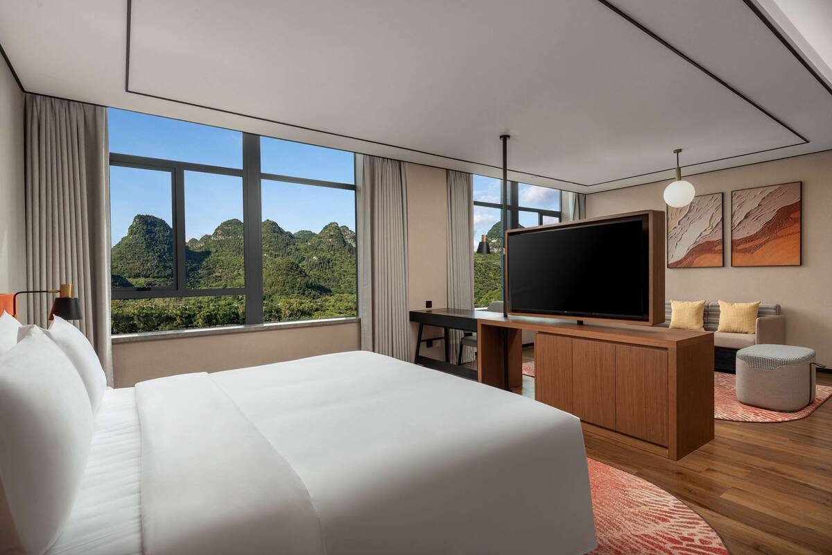 Camera d'hotel moderna con un letto grande, una scrivania, una TV a schermo piatto e vista sulle montagne verdi.