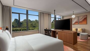 Une chambre d’hôtel moderne dotée d’un grand lit, d’un bureau, d’une télévision à écran plat et offrant une vue sur des montagnes verdoyantes.