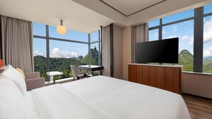 Una habitación de hotel moderna con una cama grande, un televisor, un escritorio con una silla y vistas a las montañas.