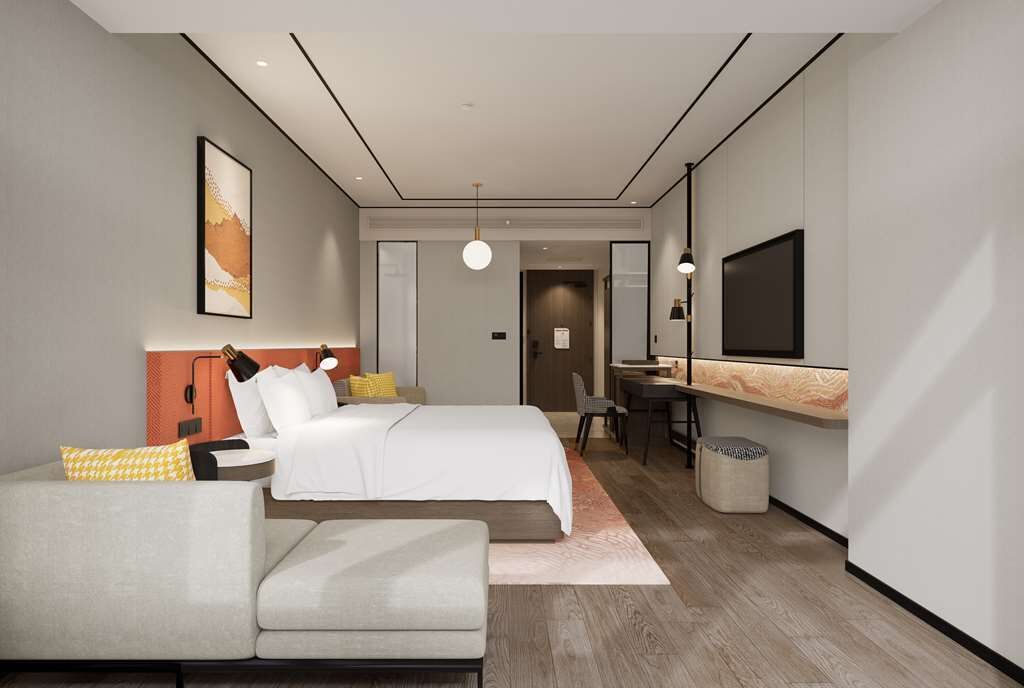 A modern hotel room with a bed, a desk, a chair, a sofa, and a TV.
