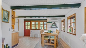 A dining area with a wooden table and chairs, a window with a view of greenery, and a kitchen area with wooden cabinets and a red door. - 1 bedroom awesome home in Rudkøbing (Rudkøbing)