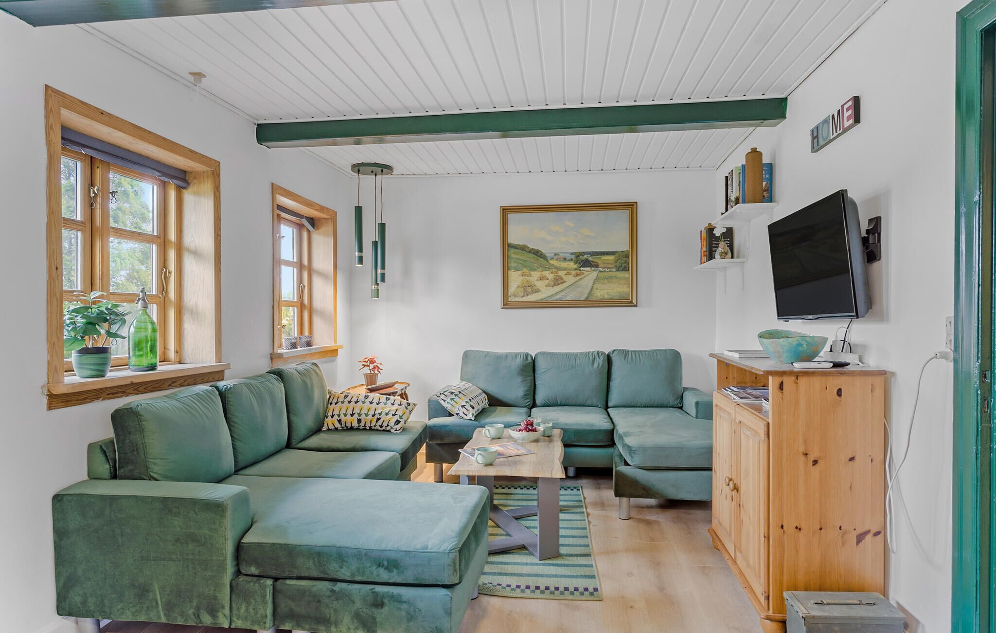A cozy living room with a green sofa set, a wooden cabinet, and a painting on the wall.
