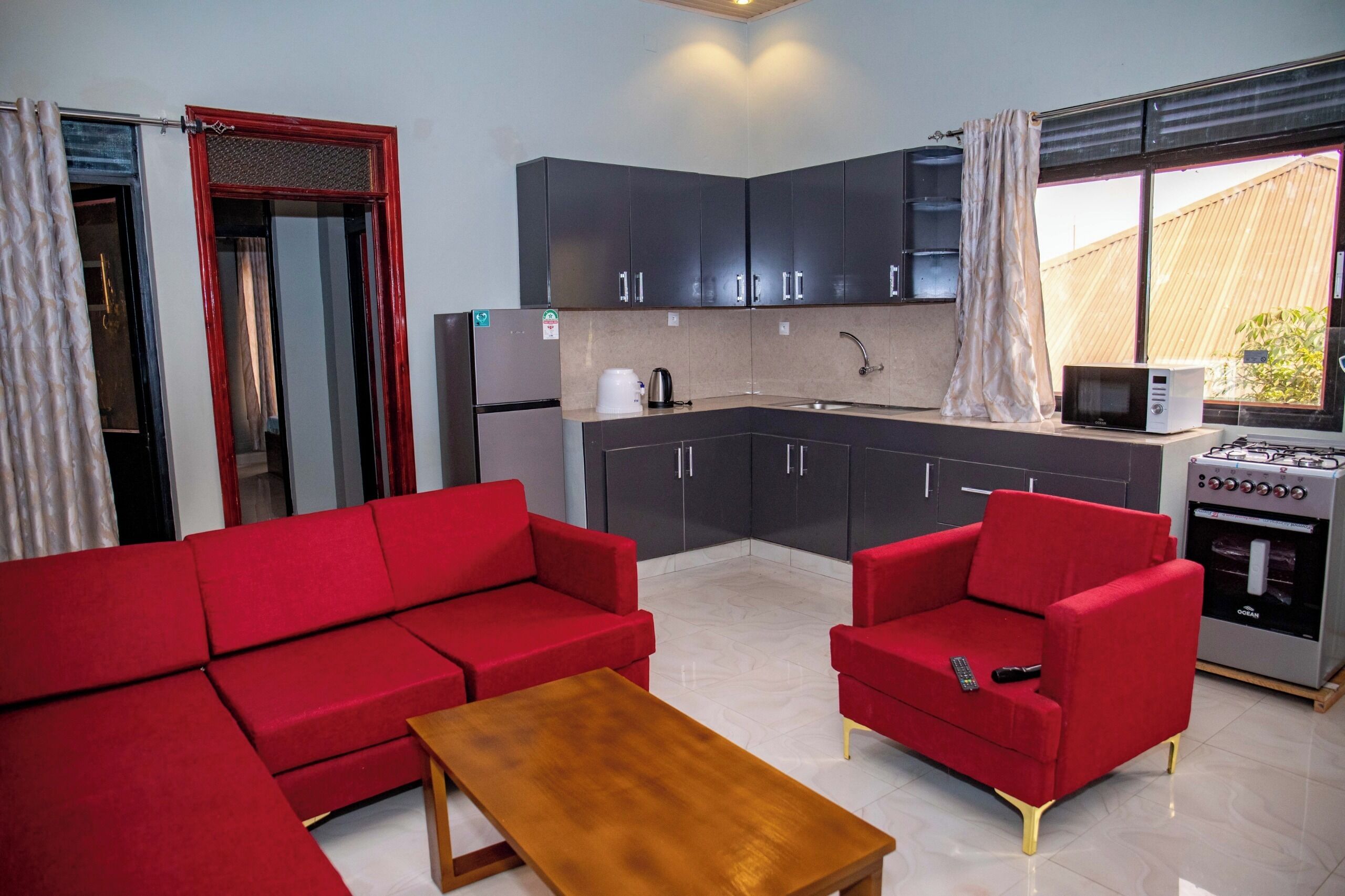 Un espace de vie compact comprenant un coin cuisine, un canapé rouge, un fauteuil rouge et une table basse en bois.
