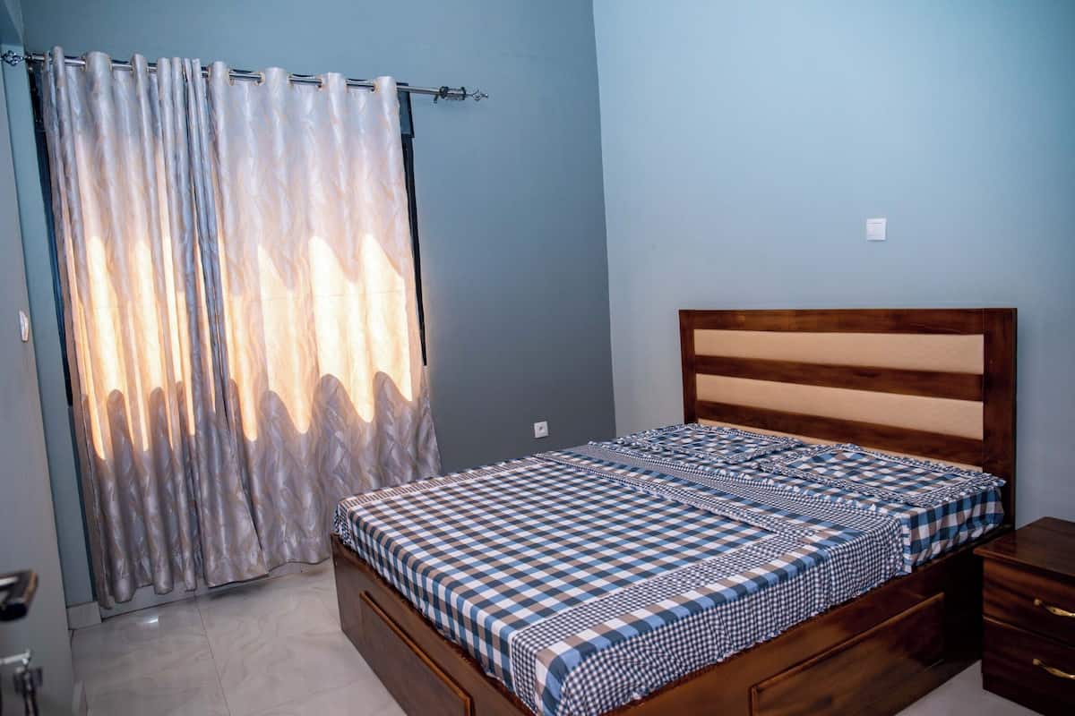 A bedroom with a bed, wooden headboard, and a curtain.