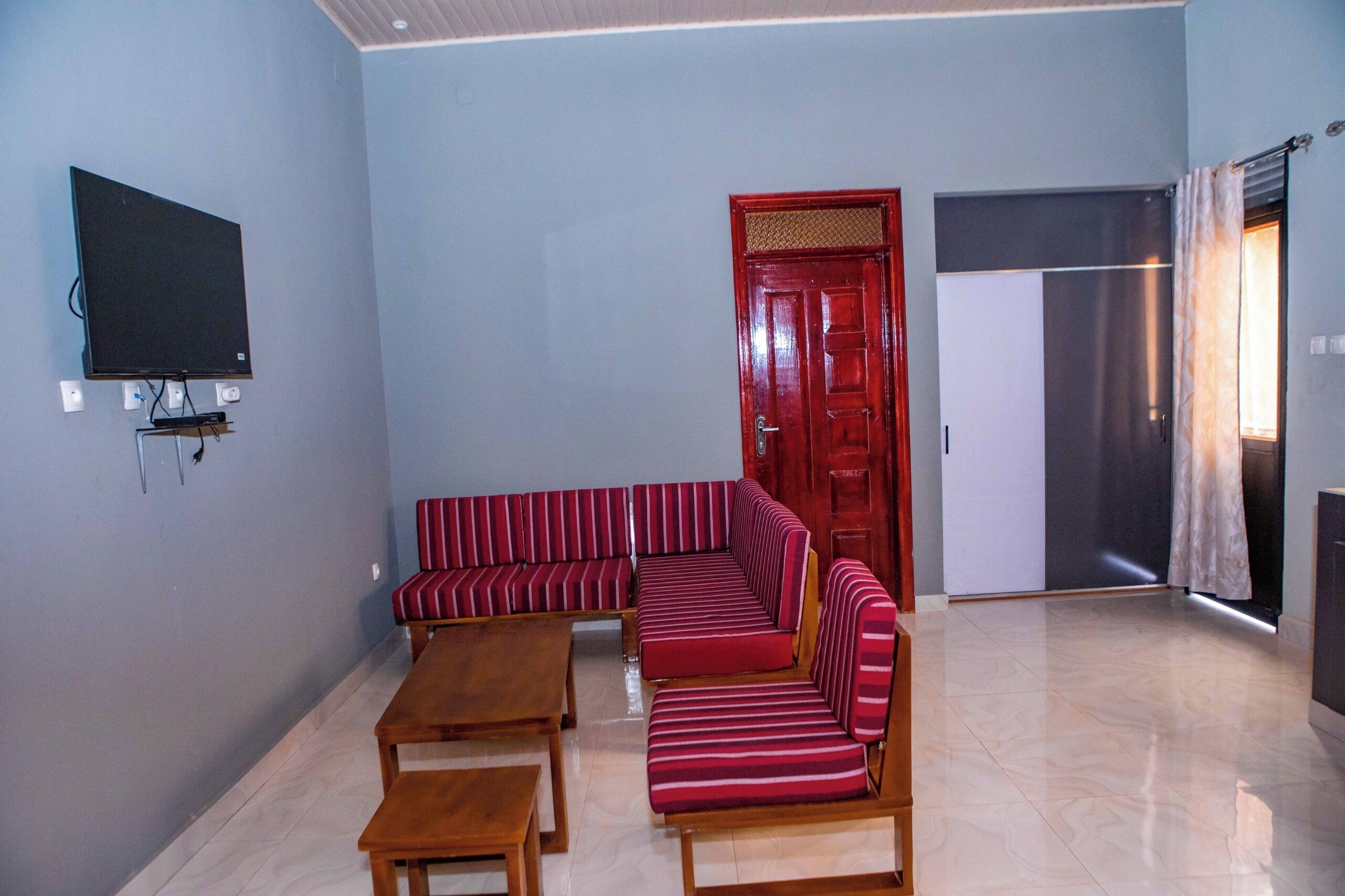 Una sala de estar con un sofá rojo a rayas, un televisor de pantalla plana montado en la pared y una mesa de centro de madera.