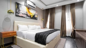 A modern bedroom with a large bed, bedside tables, an air conditioning unit, and a painting on the wall. - Vic & J Lounge and Hotel (Asaba)