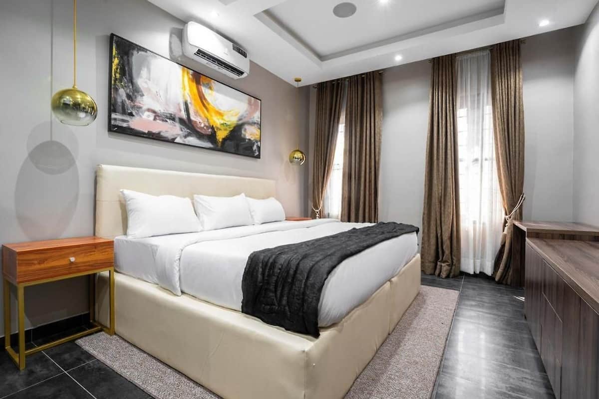 Un dormitorio moderno con una cama grande, mesitas de noche, un equipo de aire acondicionado y un cuadro en la pared.