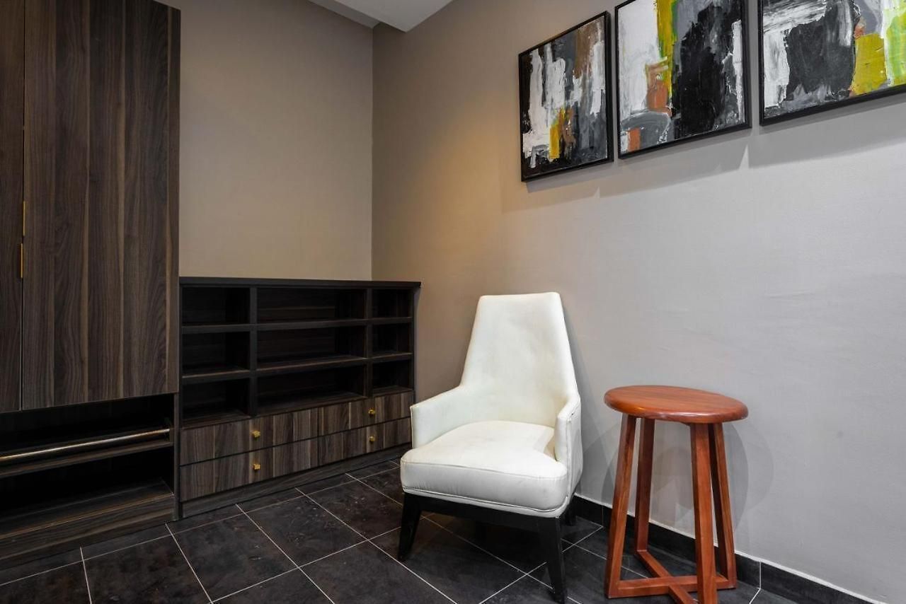 A modern interior with a white armchair, a wooden stool, a dark wood cabinet, and abstract art on the wall.