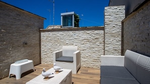 Eine Terrasse mit Korbmöbeln, einer weißen Bank und einer Vogel-Skulptur.