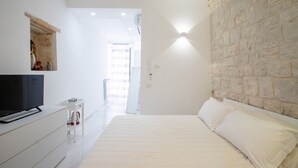 A bedroom with a bed, a TV on a dresser, a stone wall, and a bright light fixture. - GuestHost - Il Torrino al Porto Room (Bisceglie)