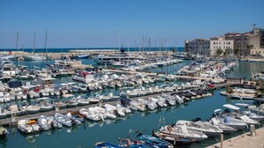 A marina with numerous boats docked, a clear sky, and buildings in the background. - GuestHost - Il Torrino al Porto Room (Bisceglie)
