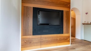A modern living room with a large flat-screen TV mounted on a wooden wall unit. - Appartamento Casa Tre Colli (Trentino-Alto Adige)