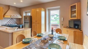 A modern kitchen with wooden cabinets, a tiled backsplash, and a dining area with a table set for two. - Appartamento Casa Tre Colli (Trentino-Alto Adige)