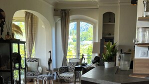 Un salón espacioso con un ventanal grande, un sillón estampado con motivos de cebra, un sofá blanco y una zona de comedor con una cafetera.