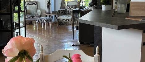 A spacious living area with a large window, a zebra-patterned chair, a white sofa, and a dining area with a coffee machine.