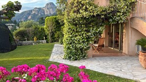 Un jardín con una planta en maceta de flores rosas y blancas, un camino de piedra y un edificio con balcón.