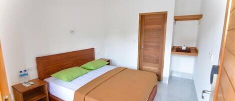 A bedroom with a wooden bed, green pillows, a wooden nightstand, a water bottle, and a wooden door.