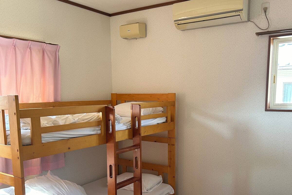 A bunk bed room with a wooden floor, a single bed, and an air conditioning unit on the wall.