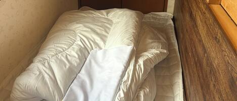 Una cama pequeña y bien hecha con ropa de cama blanca en una habitación con cabecera de madera y un armario.