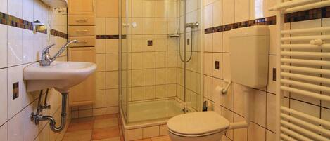 A bathroom with a shower, sink, toilet, and radiator.