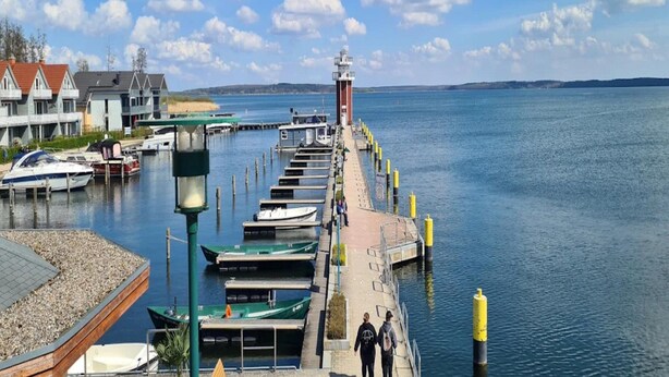 A waterfront pier with boats docked, a lighthouse, and buildings along the shore. - Ferienhaus Kiebitz, Plau am See (Plau am See)
