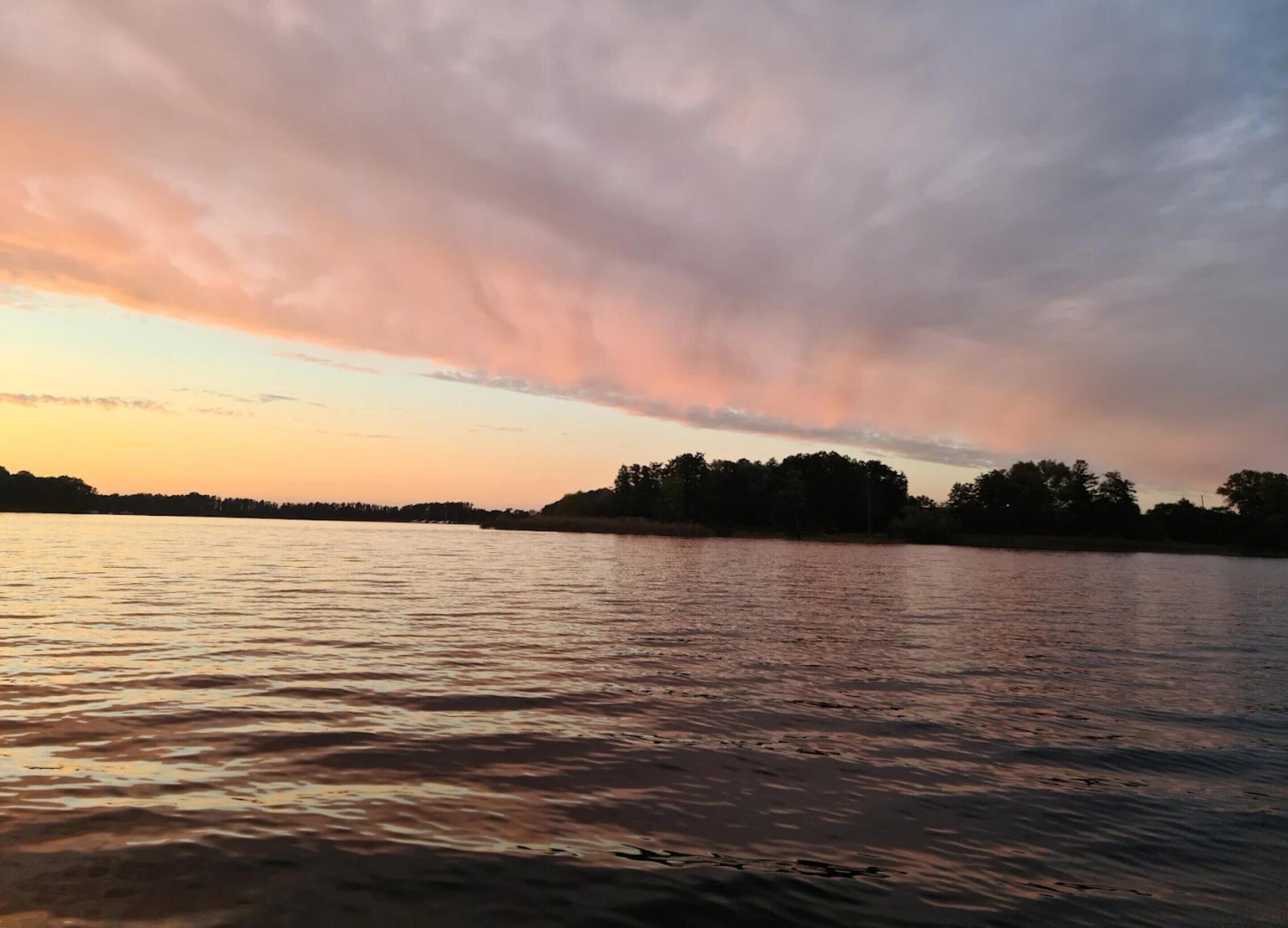A calm lake at sunset with a silhouette of trees in the background.