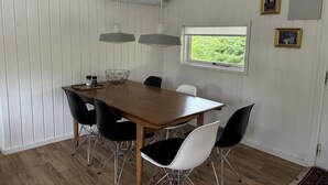 A dining room with a wooden table, black and white chairs, pendant lights, and a window with a view of greenery.