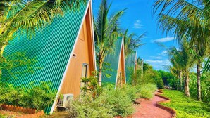 A row of modern, triangular-roofed buildings with a pathway leading through a lush, green landscape. - Xanh Homestay (Phu Cat)