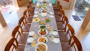 A long dining table set with various dishes, surrounded by wooden chairs. - Xanh Homestay (Phu Cat)