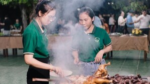 Two people grilling food outdoors with a table of dishes in the background. - Xanh Homestay (Phu Cat)