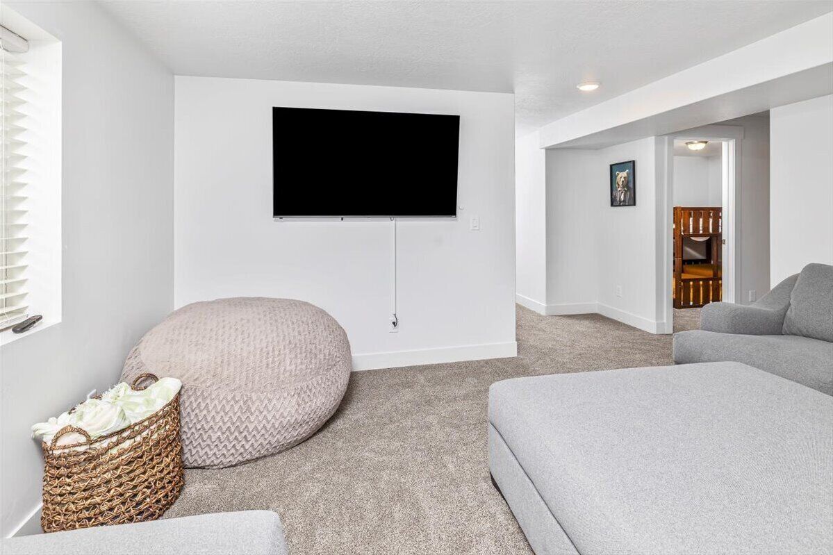 A modern living room with a flat-screen TV mounted on the wall, a grey sofa, a round bean bag, and a wicker basket.