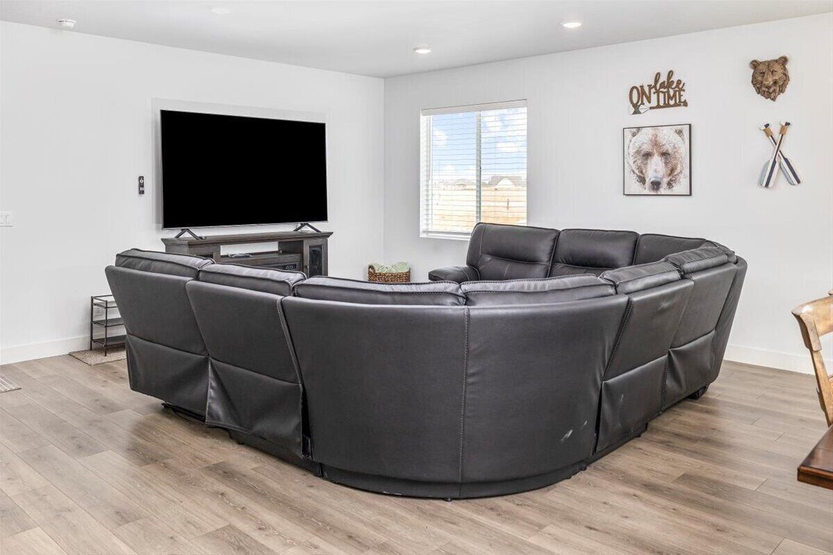 A modern living room with a sectional sofa, a flat-screen TV, and a window with blinds.