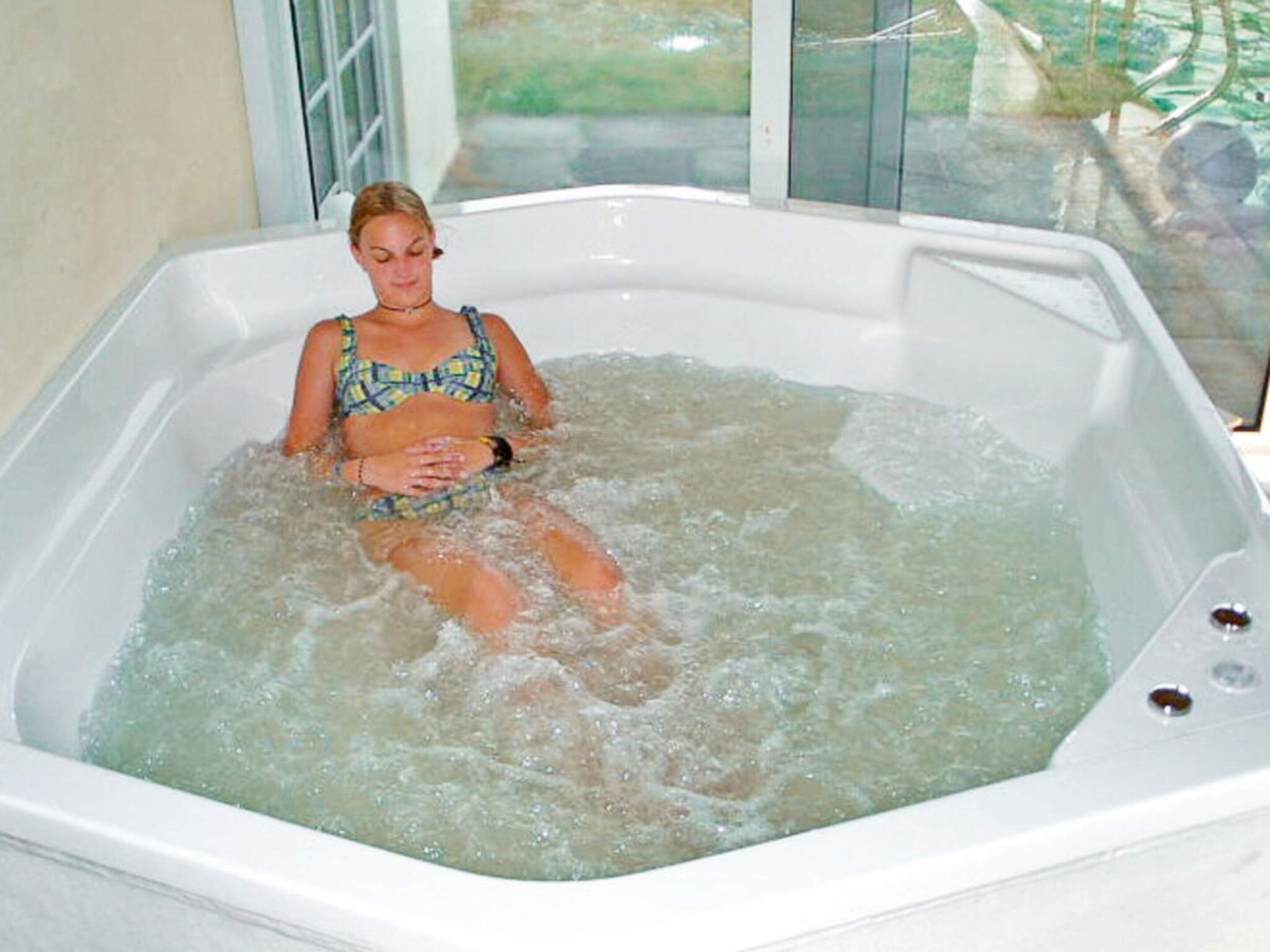A person sitting in a hot tub with a window in the background.