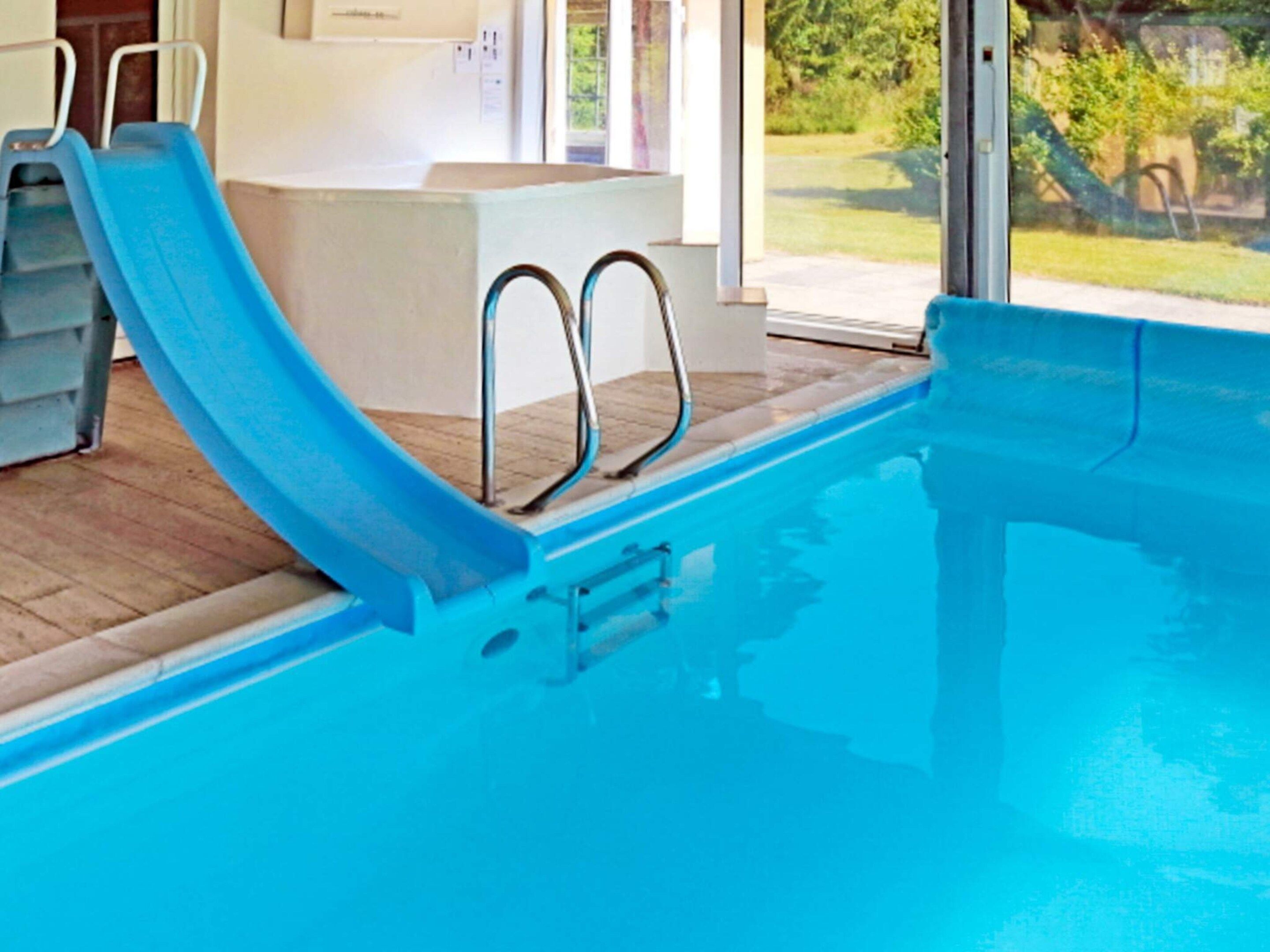 A swimming pool with a blue slide, metal handrails, and a wooden deck.