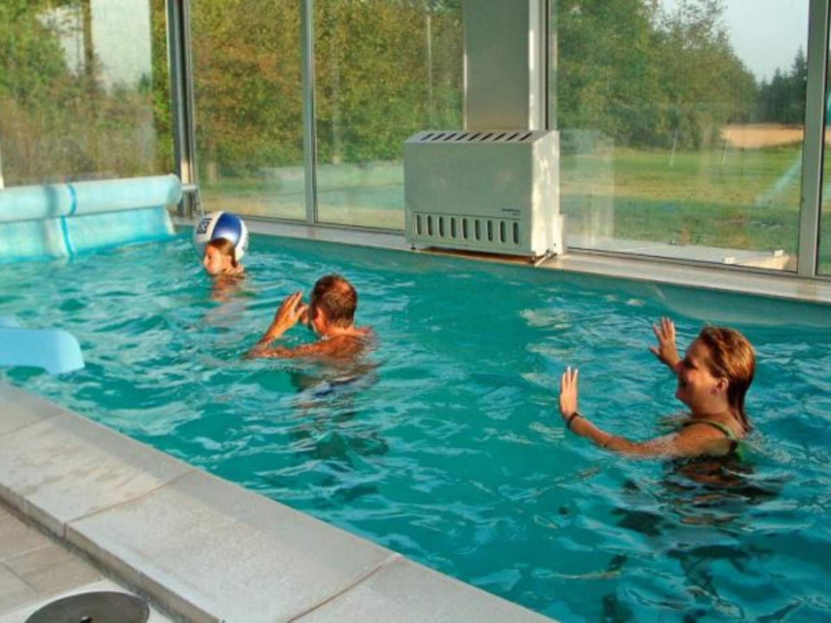An indoor swimming pool with clear glass walls, a water filtration unit, and a view of the outdoors.